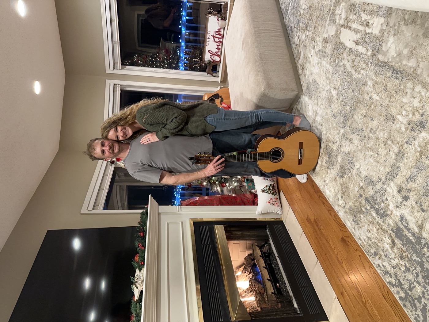 Jared and Anna by the fireplace at Christmas with two acoustic guitars