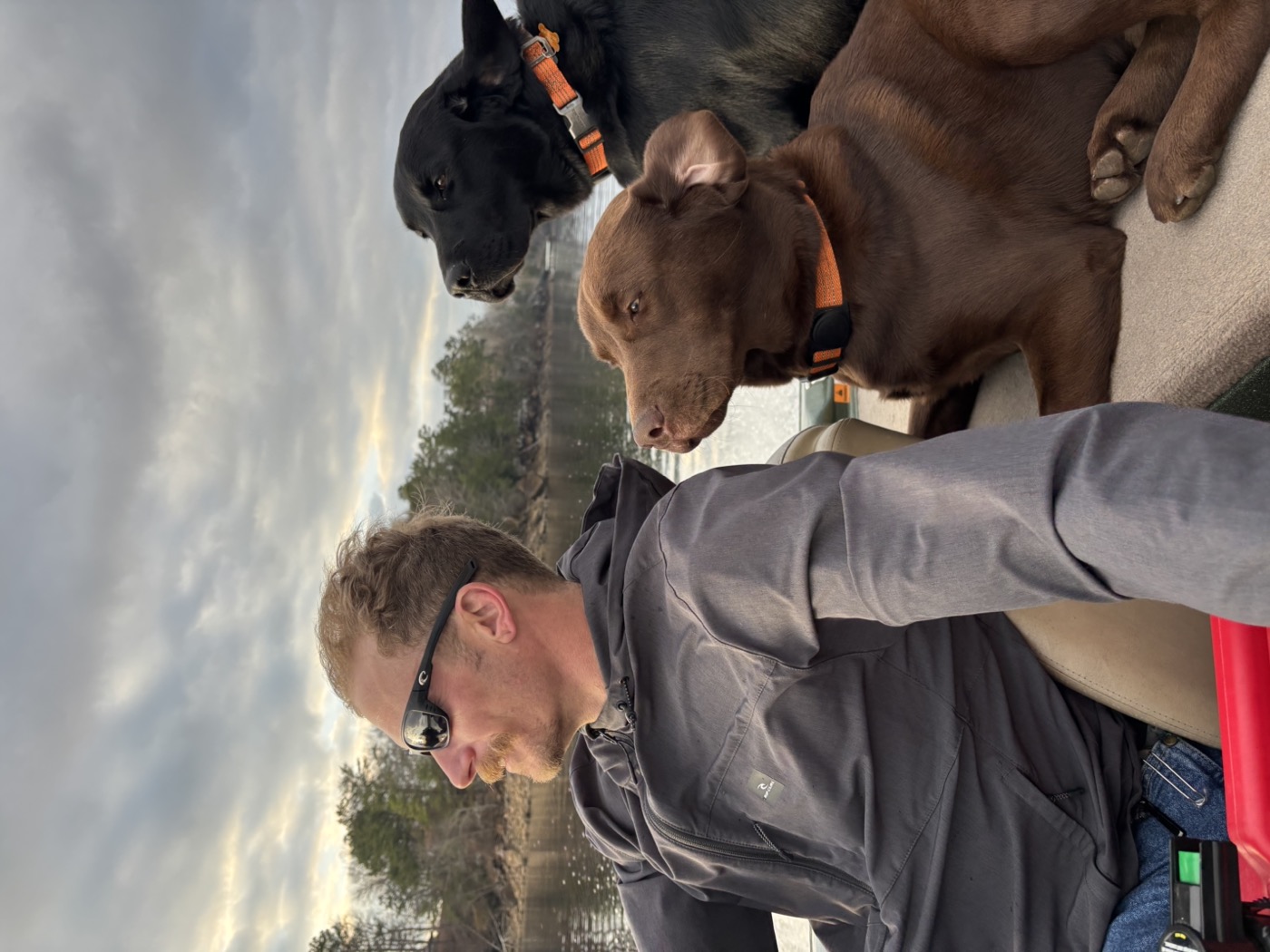 Jared at the wheel of the boat with both Labs riding along under a moody sky