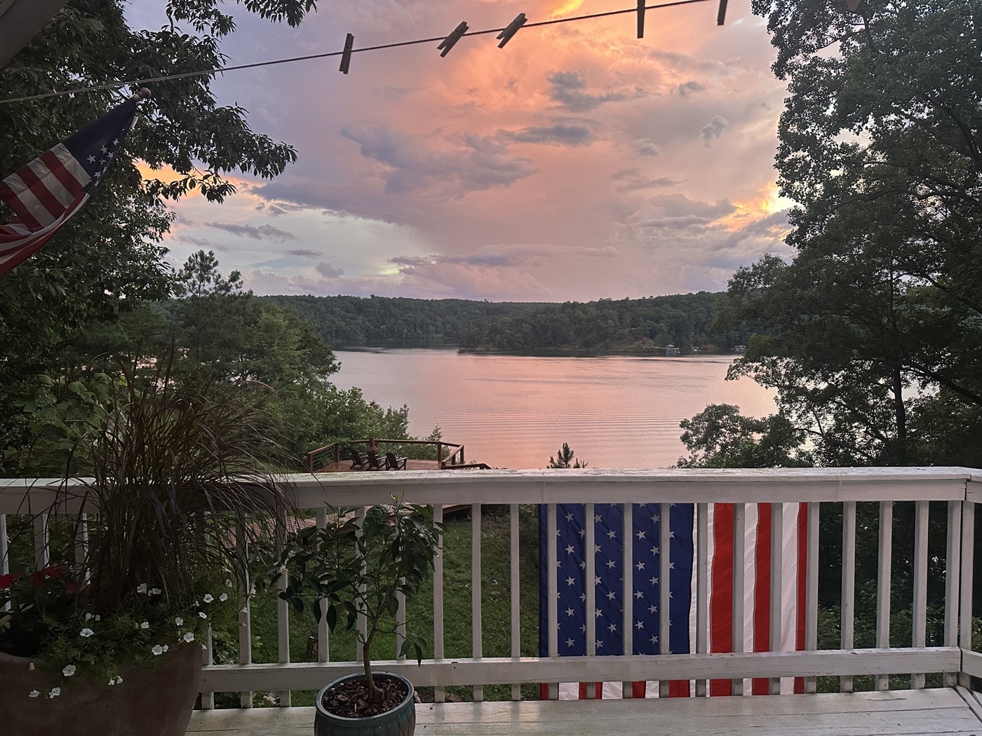 Pink sunset over the lake from a porch with American flags on the white railing