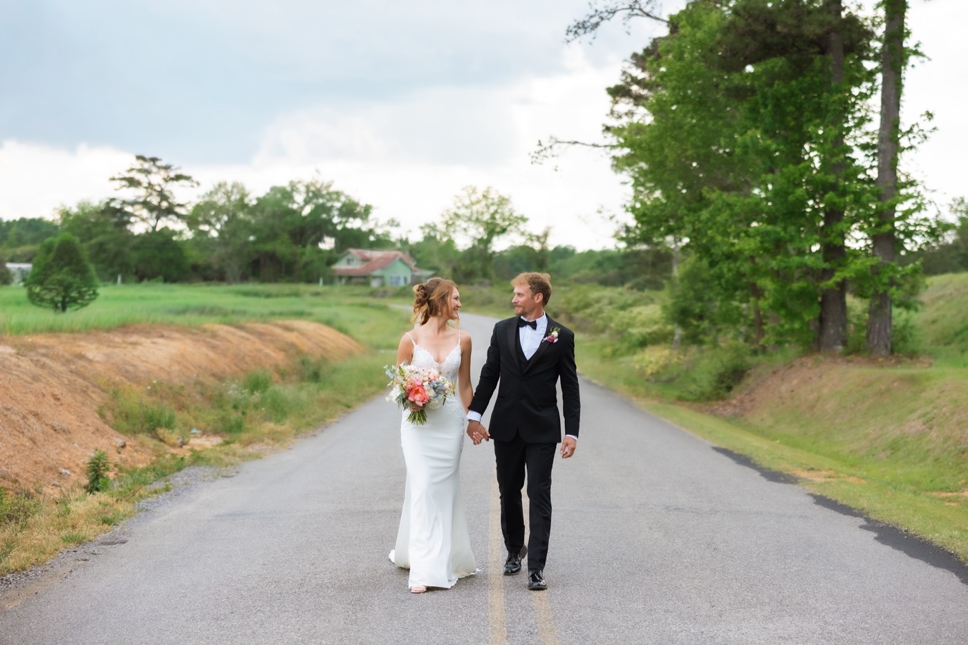 Jared and Anna in wedding clothes walking hand in hand down a country road