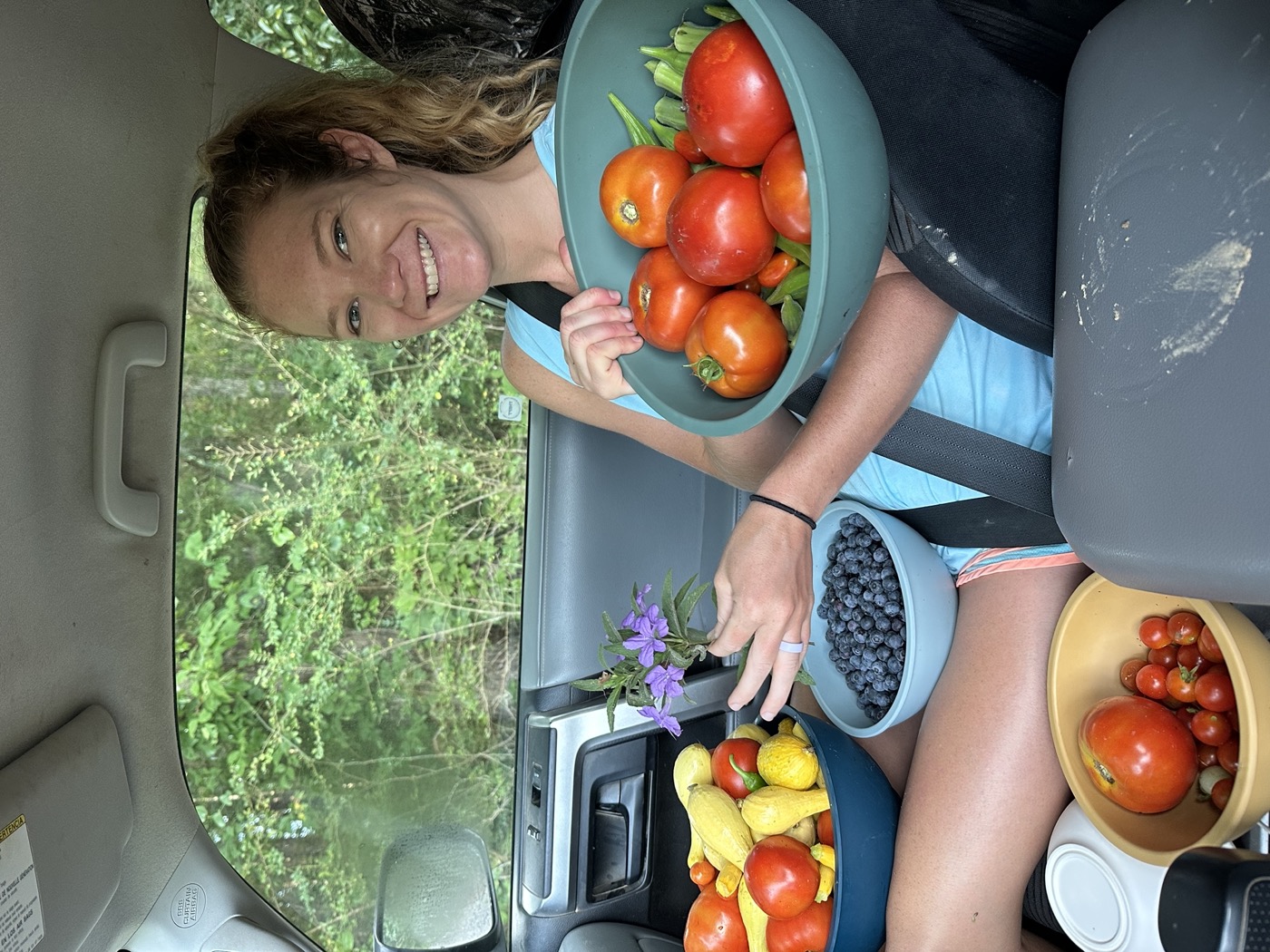 Anna in the truck holding bowls piled with tomatoes, blueberries, squash, and okra from the garden